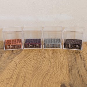 May include: Four square clear acrylic display cases, each containing a small rectangular stand with a honeycomb-patterned top. The front of each stand features the embossed text THE CORN VAULT in copper, purple, silver, and black colours.