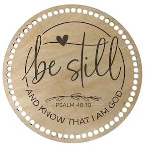 May include: A round wooden plaque with a crocheting ring around the edge. The plaque has a heart and the text "be still and know that I am God - Psalm 46:10" printed on it.