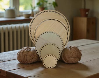 May include: A collection of unfinished wooden crochet bases in various sizes, each with evenly spaced holes for yarn. Two balls of tan yarn sit on a wooden table, complementing the natural tones of the bases. The arrangement suggests a craft project.