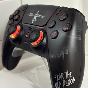 May include: Black gaming controller with the words "Bloodborne" and "Fear the Old Blood" in white. The controller has red accents around the joysticks and buttons. The controller is designed for video games.