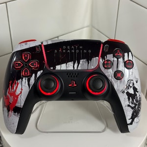 Könnte beinhalten: Benutzerdefinierter schwarz-weißer PlayStation 5-Controller mit roten Akzenten. Der Controller zeigt den Text "DEATH STRANDING" und ein grafisches Design mit roten Spritzern und einer Charakterillustration. Die Tasten und Joysticks sind rot beleuchtet.