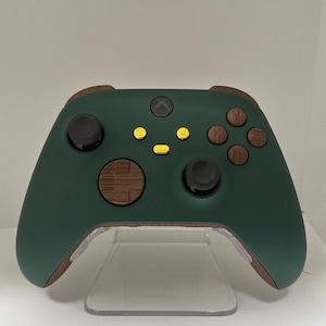 May include: A dark green Xbox controller with brown wooden accents. The controller has yellow buttons and a black Xbox logo.