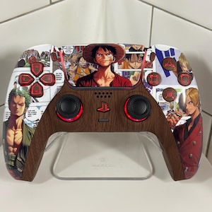 May include: A custom video game controller with a wood-effect centre and a white top surface decorated with manga illustrations. The buttons are red, and the controller is displayed on a clear stand.