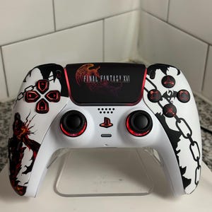 Könnte beinhalten: Weiß-schwarzer Gaming-Controller mit roten Akzenten. Der Controller zeigt den Text "FINAL FANTASY XVI" und eine Grafik eines Phönix. Die linke Seite hat eine Charaktergrafik und die rechte Seite ein Kettenmuster.