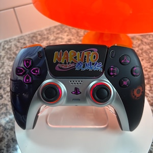 以下が含まれることがあります： NARUTOをテーマにしたカスタムPlayStationコントローラー。 コントローラーは、紫と赤のアクセントが付いた黒とシルバーのデザインです。 上部にはNARUTOのロゴが大きく表示され、側面にはキャラクターアートが描かれています。