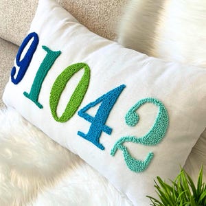 Peut inclure: Un oreiller blanc avec les chiffres 91042 brodés en perles bleues, vertes et turquoise.