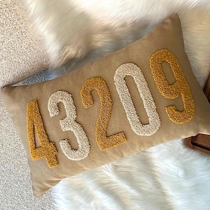 Könnte beinhalten: Ein beiger Kissenbezug mit der Nummer "43209", die in weiß und gelbem Garn gestickt ist.