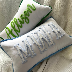 May include: Two white rectangular throw pillows with embroidered names. One pillow has the name "Allison" in green script with a green border. The other pillow has the name "Minnie" in white and light blue with a blue border.