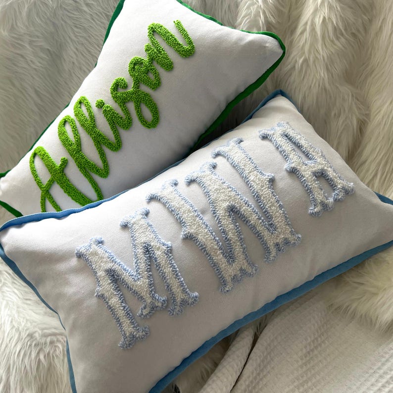 May include: Two white rectangular throw pillows with embroidered names. One pillow has the name "Allison" in green script with a green border. The other pillow has the name "Minnie" in white and light blue with a blue border.