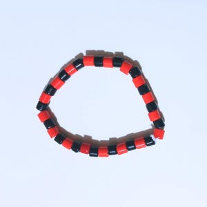 May include: A bracelet made of alternating red and black square beads. The beads are strung together to form a flexible band. The beads are a vibrant red and a deep black colour. The bracelet is a simple, yet striking accessory.