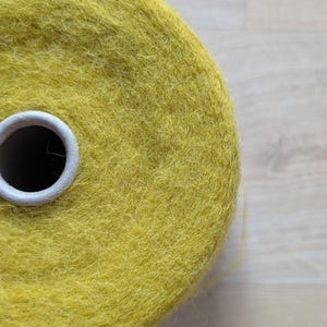 May include: Close-up of a large spool of yellow yarn. The yarn is a vibrant, solid color and appears soft and textured. The spool has a white cardboard core. The yarn is likely used for knitting or crocheting projects.