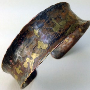 May include: A wide, hammered copper bracelet with a textured surface and a mix of gold, copper, and black tones.
