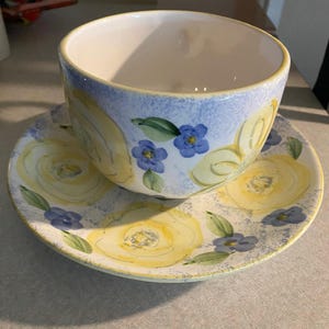 May include: A blue and white teacup and saucer set with a floral pattern of yellow roses and blue flowers.