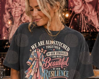 Puede incluir: Una camiseta gris carbón con un gráfico de un abrigo estilo patchwork, una mariposa y el texto: WE ARE ALL STITCHED TOGETHER BY OUR STRUGGLES AND MADE BEAUTIFUL BY OUR RESILIENCE Dolly Parton. El diseño incluye estrellas y corazones.