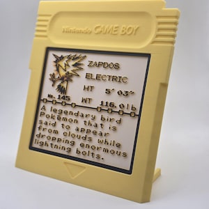 May include: A yellow Game Boy cartridge-shaped display featuring the text "Nintendo GAME BOY." The display includes information about the Pok&eacute;mon Zapdos, including its height of 5' 03" and weight of 116.0 lbs.