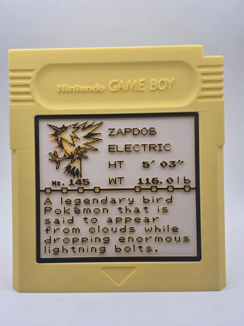 May include: A yellow Nintendo Game Boy cartridge featuring a Zapdos Pok&eacute;mon card design. The card includes the text "ZAPDOS ELECTRIC" and details about the Pok&eacute;mon's height and weight, 5' 03" and 116.0 lb, respectively. The cartridge has a black border.