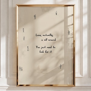 May include: A rectangular wall art print in a gold frame featuring a beige background with small black line-drawn figures scattered around the edges and the black text: Love, actually, is all around. You just need to look for it.