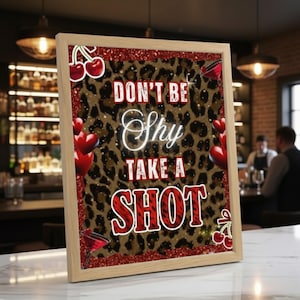 以下が含まれることがあります： ヒョウ柄の背景に「DON'T BE Shy TAKE A SHOT」の文字が白と赤で書かれた額入りのサイン。赤いさくらんぼ、ハート型の風船、カクテルグラスで飾られています。