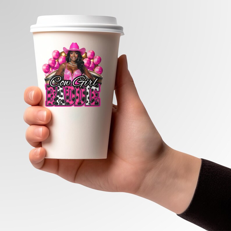 K&ouml;nnte beinhalten: Ein wei&szlig;er Pappbecher mit einer Grafik einer Frau in einem rosa Cowboyhut und -outfit, mit dem Text "Cow Girl Baddie" in Rosa und Schwarz. Rosa Ballons sind im Hintergrund.