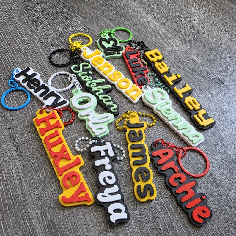 May include: A collection of colorful silicone keychains featuring raised lettering in various fonts and colors, including names such as Henry, Jenson, Siobhan, Luke, Bailey, Sienna, Huxley, Freya, James, and Archie, each attached to a metal ring.