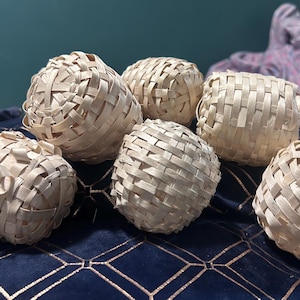 May include: Six woven, light brown, decorative balls on a blue and gold patterned surface. The balls are made of natural materials and have a woven texture.