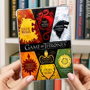 May include: A rectangular clear protective case featuring a Game of Thrones graphic design. The print displays six house sigils with mottos: Lannister, Targaryen, Stark, Martell, Greyjoy, Baratheon, and Tyrell, arranged in a colorful collage.