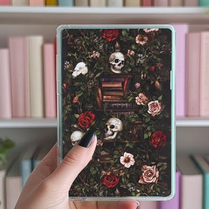 Könnte beinhalten: Eine transparente Handyhülle mit einem dunklen Hintergrund, der mit einem Blumenmuster mit roten Rosen, weißen Blüten und Schädeln verziert ist. Die Schädel sind von Büchern und Ranken umgeben.