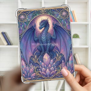 Peut inclure: Une coque de tablette transparente ornée d'une illustration vibrante d'un dragon bleu perché sur un amas de cristaux violets et roses. L'œuvre comprend une lune brillante, des filigranes dorés et le texte Wildflower&Pages sur le dragon.