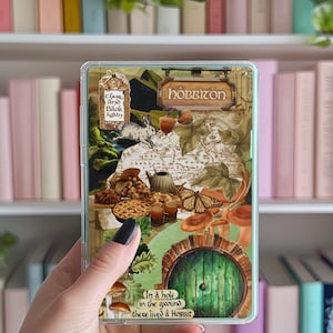 Peut inclure: Coque de téléphone transparente avec un design inspiré du Hobbit. L'illustration comprend une carte, une porte verte, des champignons et le texte "In a hole in the ground there lived a Hobbit."