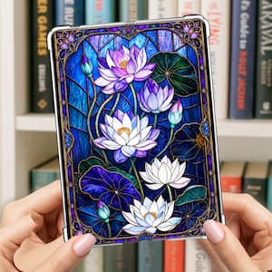 Pode incluir: Uma capa retangular para tablet com um design vibrante de vitral de flores de lótus brancas e roxas com vitórias-régias verdes sobre um fundo azul profundo. A arte é cercada por uma borda decorativa com padrões geométricos complexos.