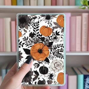Op de afbeelding: Een doorzichtige telefoonhoes met een witte achtergrond, versierd met een patroon van oranje pompoenen, zwarte en grijze bloemmotieven en een witte roos. De hoes heeft een lichtgroene rand.