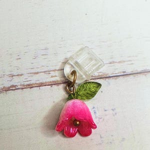 May include: A pink flower charm with a green leaf, attached to a clear plastic clip.