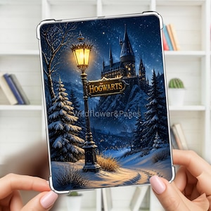 Puede incluir: Una funda transparente para tableta con una escena invernal, una farola iluminada, un letrero que dice HOGWARTS y un gran castillo al fondo. La imagen muestra pinos cubiertos de nieve y un cielo estrellado, con el texto Wildflower&Pages.