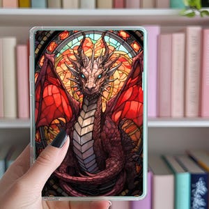Può includere: Un drago rosso e viola con occhi blu è raffigurato in stile vetrata. Il drago è circondato da una cornice circolare in vetro colorato con colori rosso, arancione e giallo.