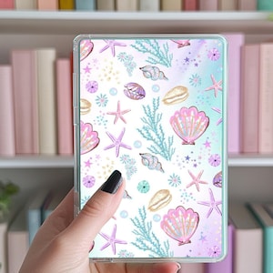 May include: A clear phone case with a white background and a pattern of pink and blue seashells, starfish, and seaweed.
