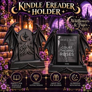 May include: A black e-reader holder featuring bat-like wings on the sides and a mountain, moon, and star relief design. One holder is empty, while the other displays a Kindle e-reader showing the book cover for Court of Thorns and Roses.