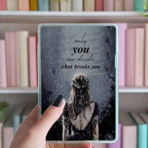 May include: A clear phone case featuring a dark illustration of a woman with long hair and a detailed black dress. The text "only you can decide what breaks you" is displayed in a stylized font. The case is held in front of a bookshelf.