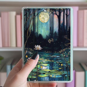 May include: A clear phone case with a colorful stained glass design of a moonlit forest scene with a pond and lily pads. The design features a full moon, trees, and water with a green, blue, and gold color scheme.