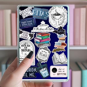 Op de afbeelding: Een transparante telefoonhoes met verschillende kleurrijke stickers met citaten en illustraties uit de boekenserie "A Court of Thorns and Roses". De stickers bevatten een boekclub-lidmaatschapskaart, een theehuislogo en een citaat over sterren en dromen.