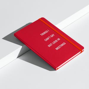 May include: Red notebook with a red ribbon bookmark. The cover has the text "Things I Can't Say Out Loud In Meetings".