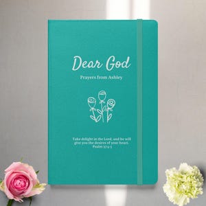 Può includere: Un diario blu turchese con una scritta bianca che recita "Dear God Prayers from Ashley" e un disegno a linea bianca di tre rose. L'iscrizione include anche un versetto biblico: "Take delight in the Lord, and he will give you the desires of your heart. Psalm 37:4-5"
