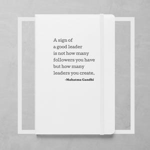 May include: A white notebook with a quote by Mahatma Gandhi: "A sign of a good leader is not how many followers you have but how many leaders you create."