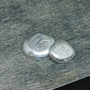 Close‑up of 999 fine silver grain shot pieces displayed on a light neutral surface beside a bamboo block. Each grain shows smooth rounded edges and bright metallic luster, highlighting purity and craftsmanship. Ideal for jewelry making, casting, or refining, these fine silver granules reflect light beautifully and emphasize the clean, modern aesthetic of artisan materials.
