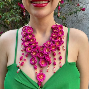 May include: A pink flower necklace with crystal accents. The necklace is layered and features a cascading design.