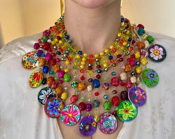 May include: A vibrant, multi-strand necklace with colorful beads and dangling, painted floral medallions. The necklace features a variety of colors, including red, yellow, green, and purple. Matching pink earrings complete the look, creating a bold and artistic statement.