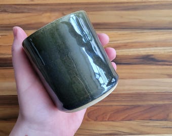 May include: A dark green ceramic mug with a light green rim. The mug is glazed and has a glossy finish.