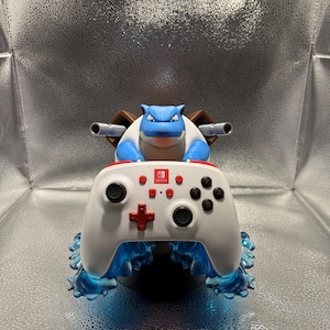 May include: A white Nintendo Switch controller with red accents, featuring a blue and brown character design. The controller has a stylized blue water effect at the bottom. The character has two cannons on its back.