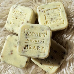 May include: Four square-shaped bars of soap with the text "Annie's Handmade Heart" embossed on each bar. The bars are a light beige color with brown flecks throughout.