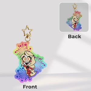 May include: An acrylic keyring featuring a cartoon character with long blonde hair and a red suit, set against a vibrant rainbow background with firework and star motifs. The charm includes a gold-coloured star-shaped clasp at the top.