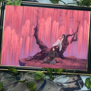 May include: Framed art print featuring a fantasy scene with two figures under a weeping tree with pink foliage. The artwork is set in a black frame with a gold inner edge, surrounded by green leafy vines.
